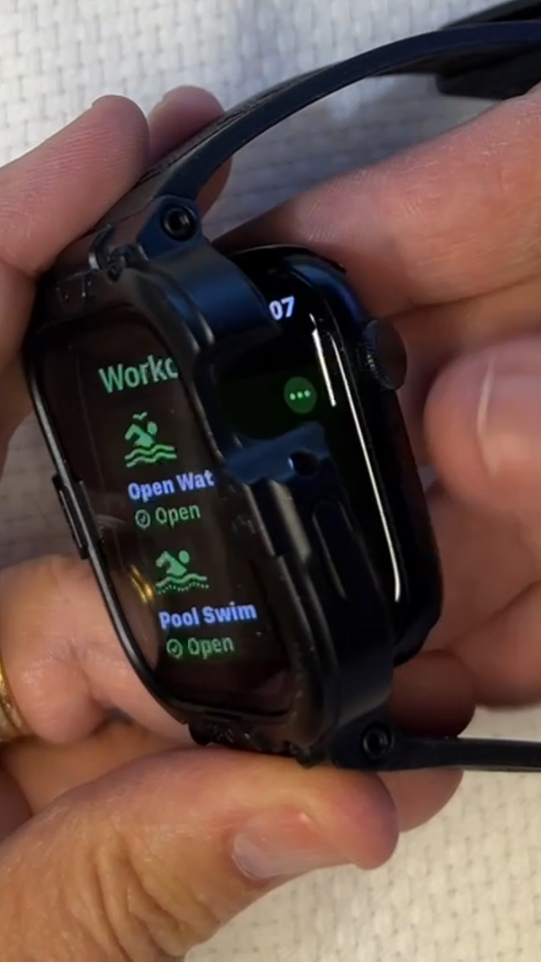 Rugged Apple Watch band on a wrist with water droplets beside a pool towel