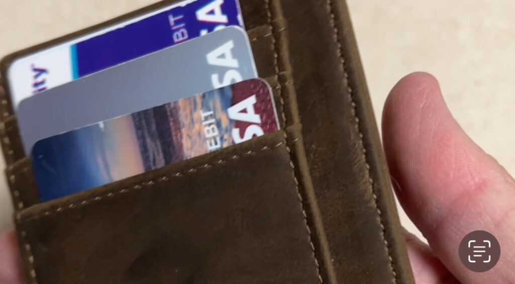 Slim wallet credit card holder with cards and folded cash on a table next to a phone