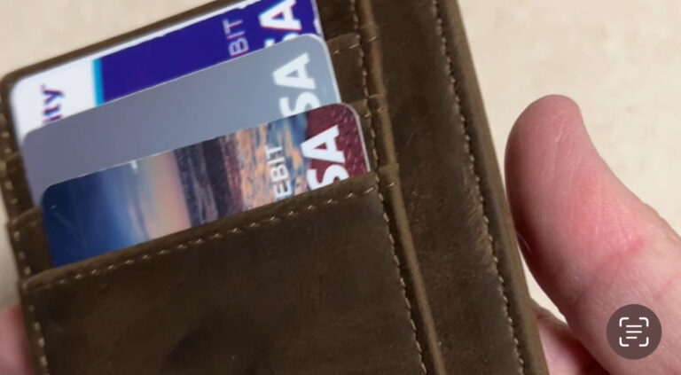 Slim wallet credit card holder with cards and folded cash on a table next to a phone