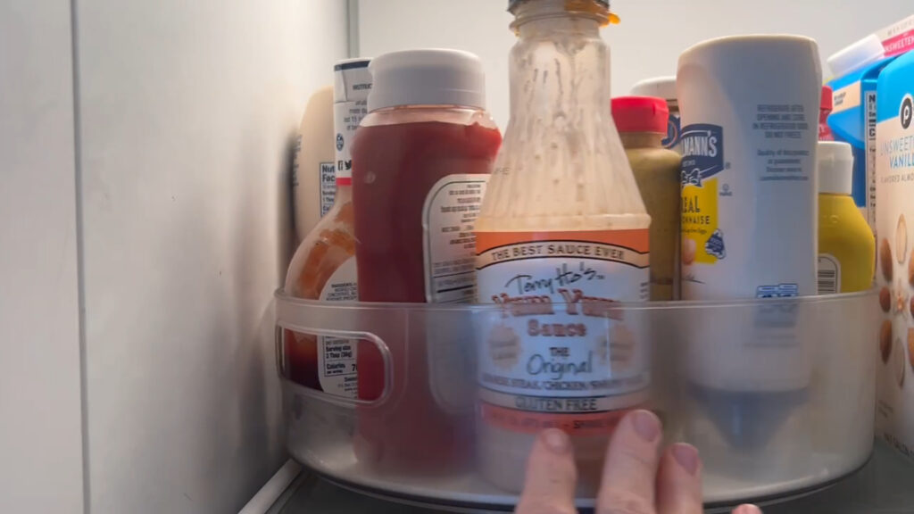 Clear Lazy Susan organizer with condiments in fridge.