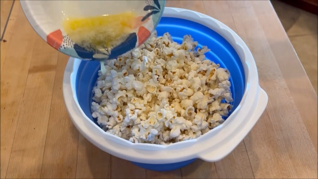 Collapsible silicone microwave popcorn bowl with lid filled with popcorn.