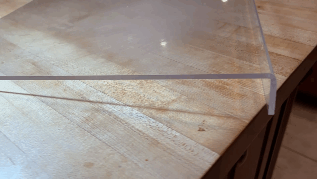 Clear acrylic cutting board with counter lip edge on kitchen counter.