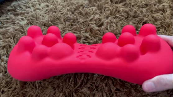 Person using silicone trigger point massager on lower back while lying on yoga mat.